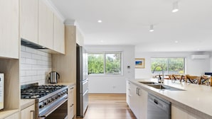 A modern kitchen with wooden cabinets, a stainless steel stove, and a dishwasher. - Cosmopolitan Sorrento (Sorrento)