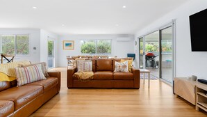 A spacious living room with a brown leather sofa, a wooden coffee table, and a large window offering a view of the outdoors. - Cosmopolitan Sorrento (Sorrento)