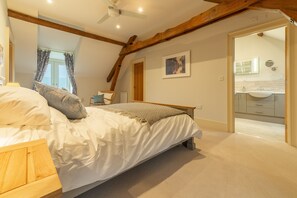 A bedroom with a bed, wooden headboard, ceiling fan, and a view into the bathroom. - Field Corner (6), Docking, Norfolk (Docking)