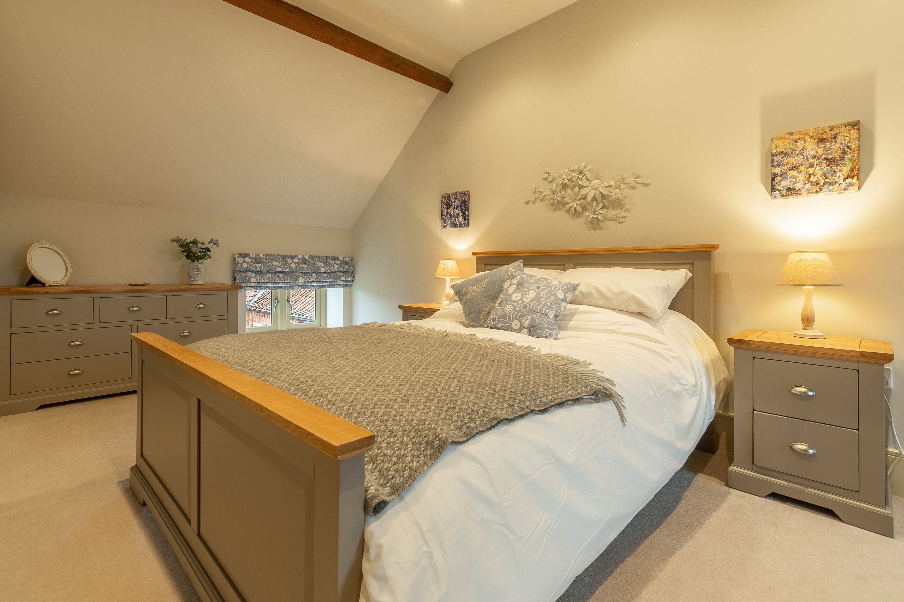 A bedroom with a bed, bedside tables, a dresser, and a window with patterned curtains.