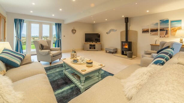A cozy living room with a sofa, armchair, and a coffee table. There is a fireplace, a television, and a window with curtains. - Field Corner (6), Docking, Norfolk (Docking)