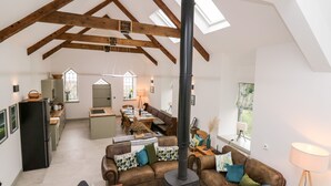 A spacious loft with exposed wooden beams, a central fireplace, a dining area, and a kitchen with a large window. - Ysgoldy Brynwyre (Llanon)