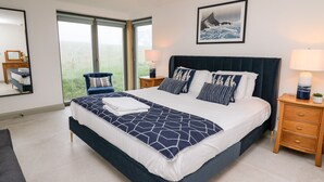 A modern bedroom with a large bed, a nightstand, a chair, and a window with a view of the outdoors. - Ysgoldy Brynwyre (Llanon)