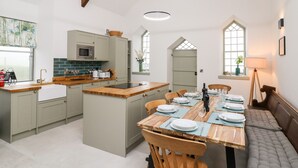 A spacious kitchen with a central island, wooden dining table set for six, and a cozy seating area with a bench. - Ysgoldy Brynwyre (Llanon)