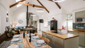 A spacious kitchen with a wooden island, a dining area with a wooden table set for six, and a loft bedroom with a large window. - Ysgoldy Brynwyre (Llanon)