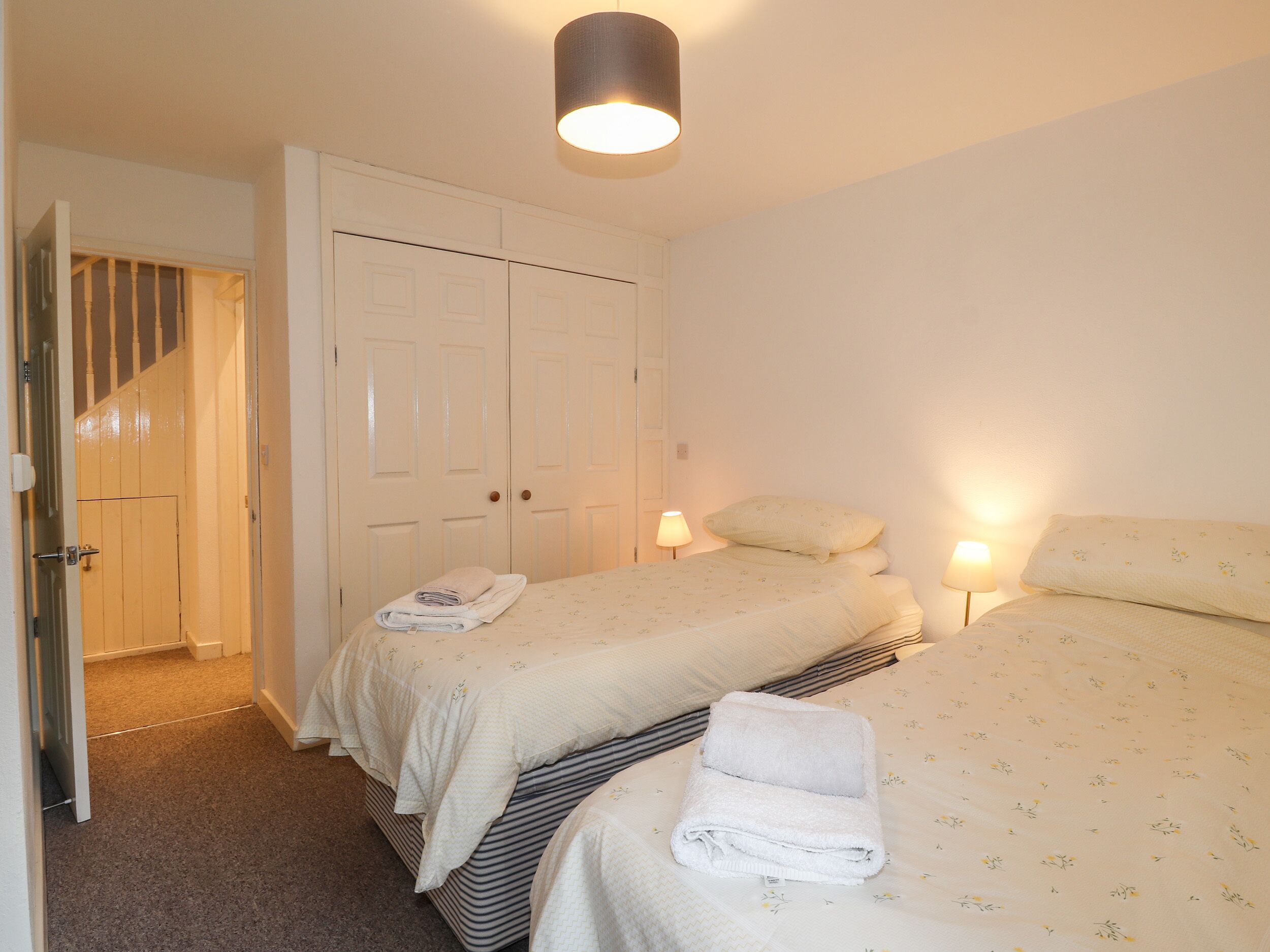 A bedroom with two beds, a wardrobe, and a door leading to a staircase.