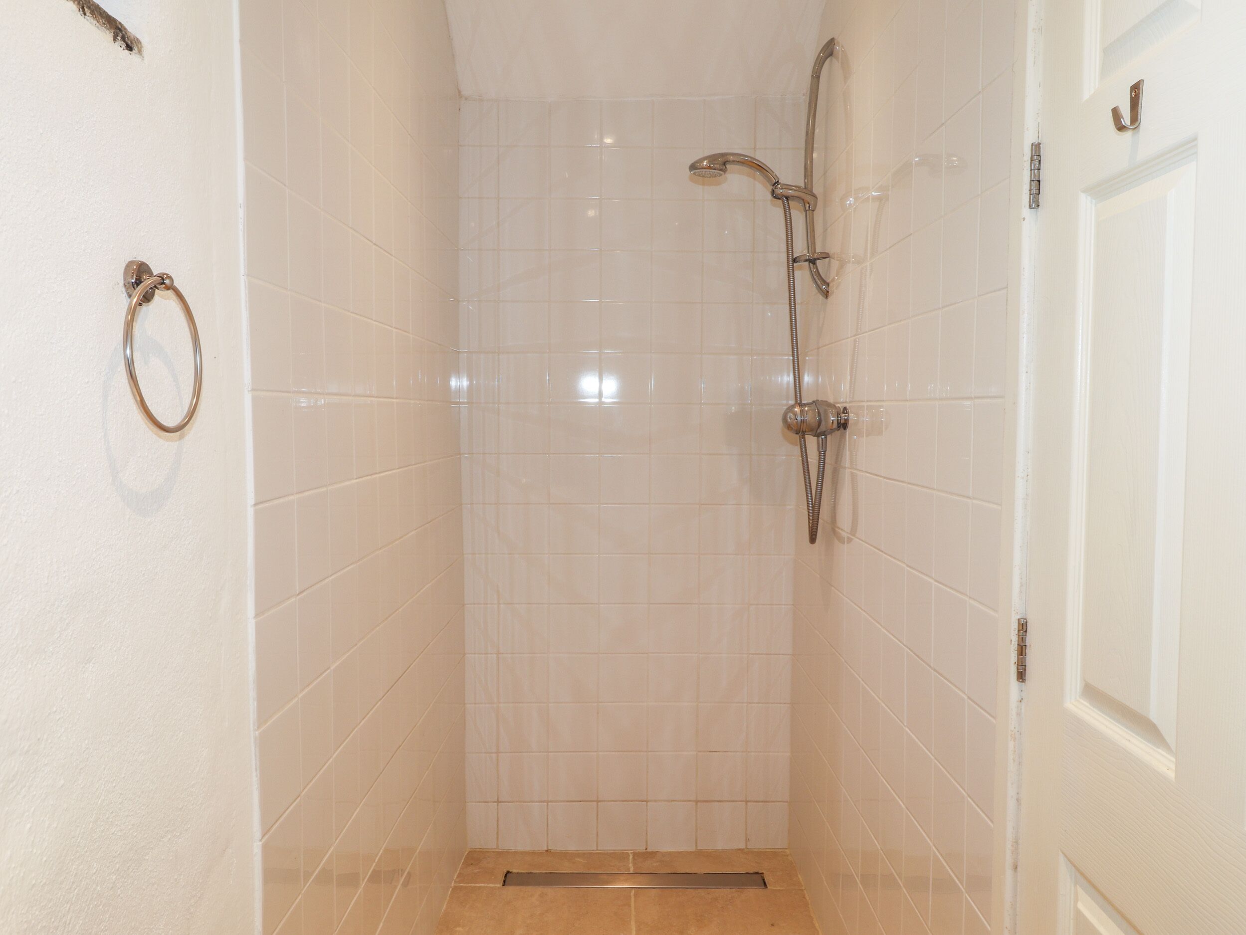 Un pequeño baño revestido con azulejos, con un cabezal de ducha y un aro para toallas en la pared.