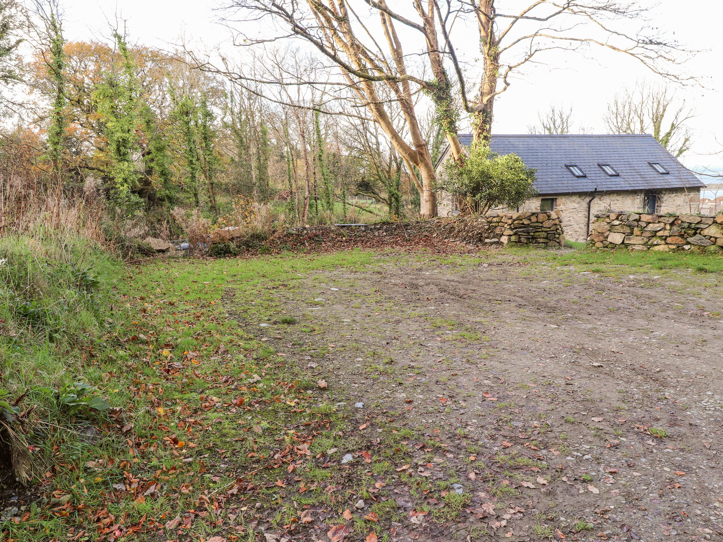 A rural property with a stone wall, a stone building with a sloped roof, and a gravel path.