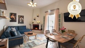 Una sala de estar con sofá, mesa de centro, chimenea, mesa de comedor preparada para cuatro comensales y televisor montado en la pared.