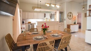 Una cocina moderna con armarios blancos, una mesa de comedor de madera preparada para cuatro comensales y un reloj grande en la pared.