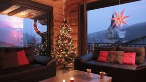 A cozy room with a Christmas tree, leather sofas, a wooden coffee table, and a view of a church with a star decoration outside.