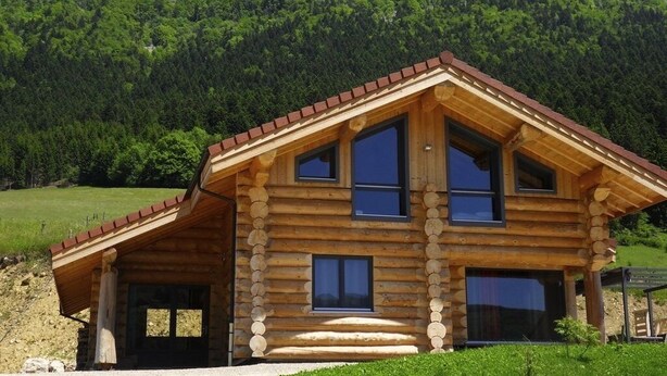A log cabin with a sloped roof, large windows, and a stone foundation.