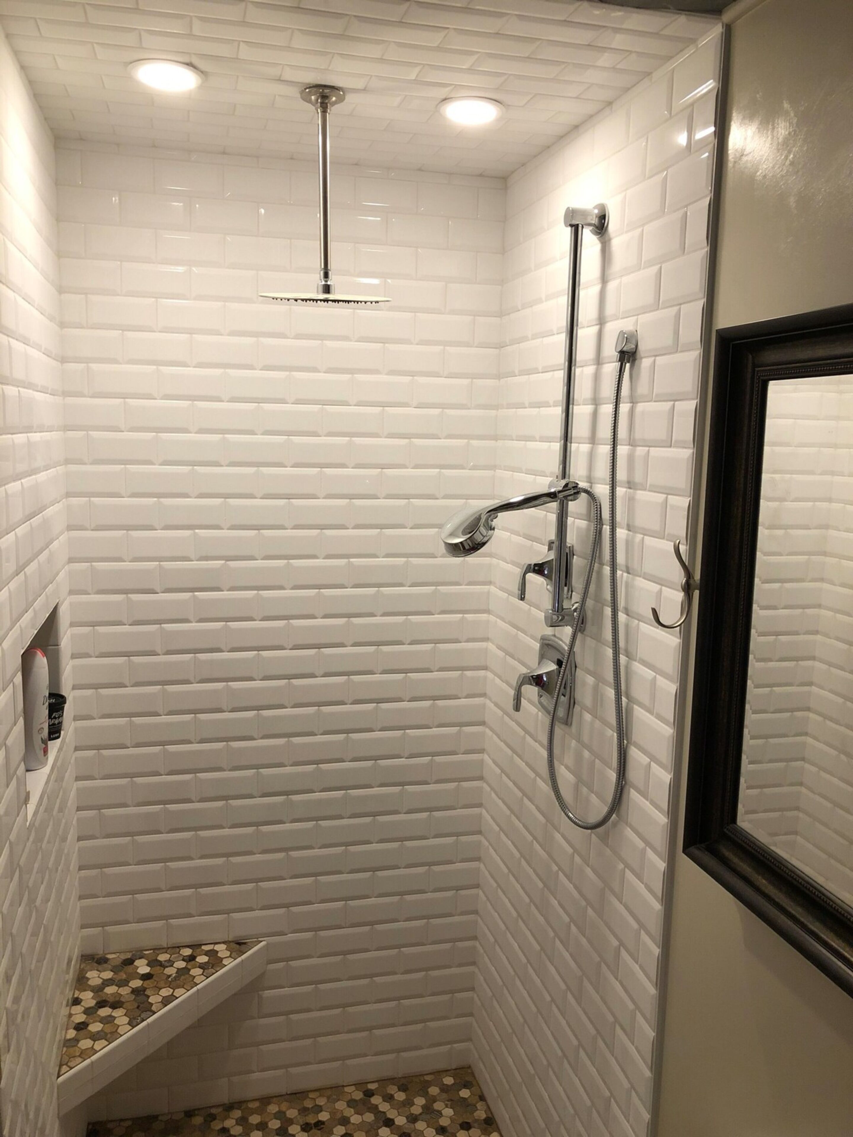 A small, tiled shower area with a showerhead, handheld shower, and a wall-mounted faucet.