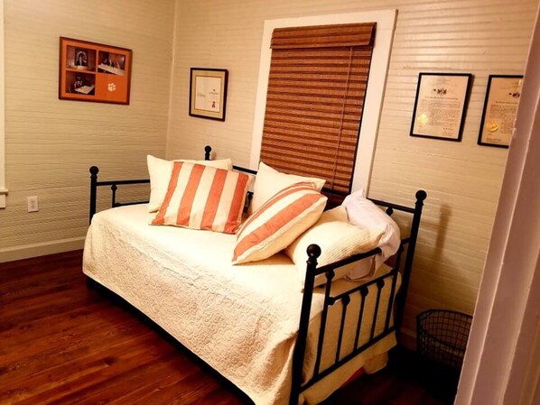 A bedroom with a bed, wooden floor, and a window with blinds.