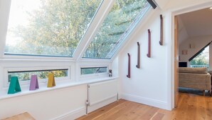 Una habitación con techo inclinado, suelo de madera, un radiador y una ventana que da a vistas de árboles.