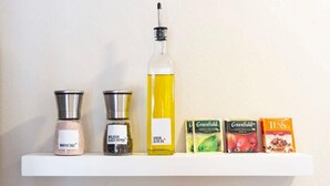 En hylla med olika föremål, inklusive en flaska olivolja, två kryddburkar och tre teförpackningar.