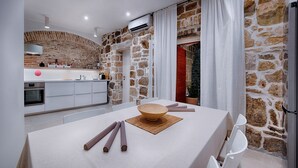Une cuisine moderne avec un mur en pierre, des meubles blancs et un coin repas avec une table dressée pour quatre personnes.