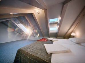 A modern hotel room with a sloped ceiling, a bed with white linens, a red blanket, and a view of the city through a skylight. - Villa Zdenka (Vis)