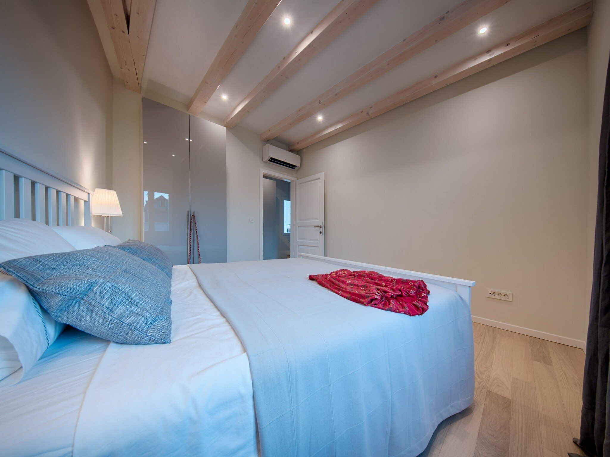 Una camera da letto con un letto, un comodino, una lampada e una coperta rossa.