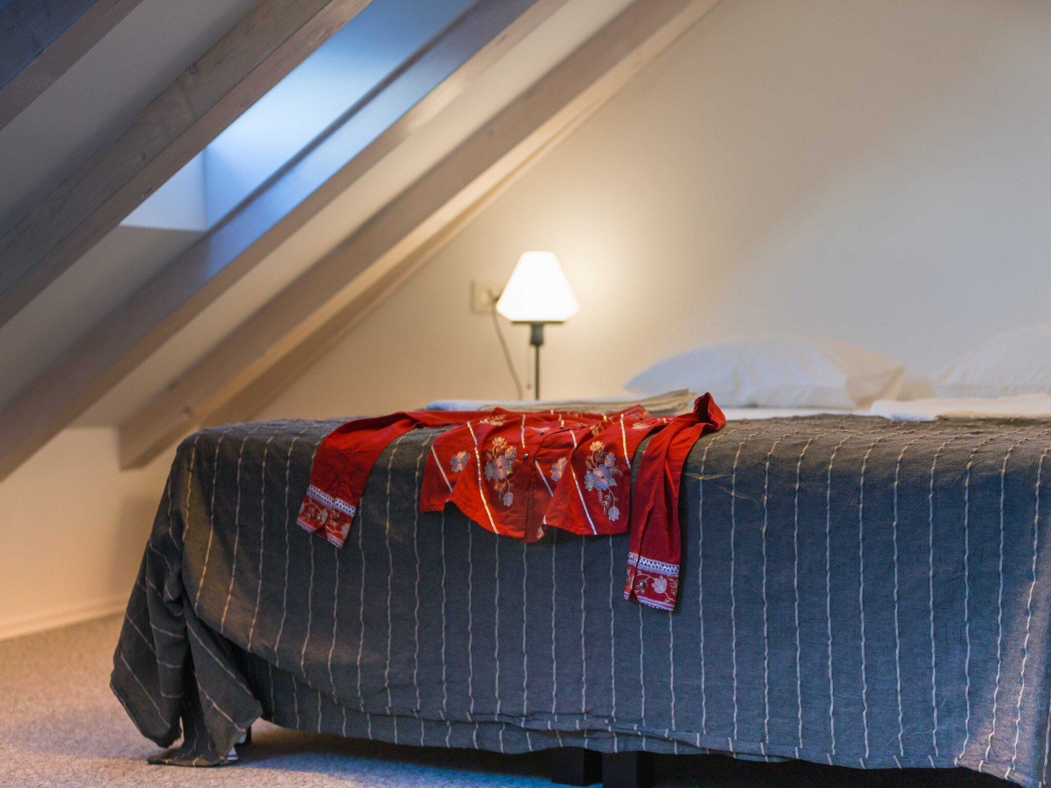 Una cama individual en una habitación con techo inclinado y una lámpara en la mesita de noche.