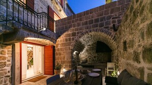 Une cour pavée de pierres, avec une table en bois dressée pour le repas, un mur en pierre et un petit coin salon.