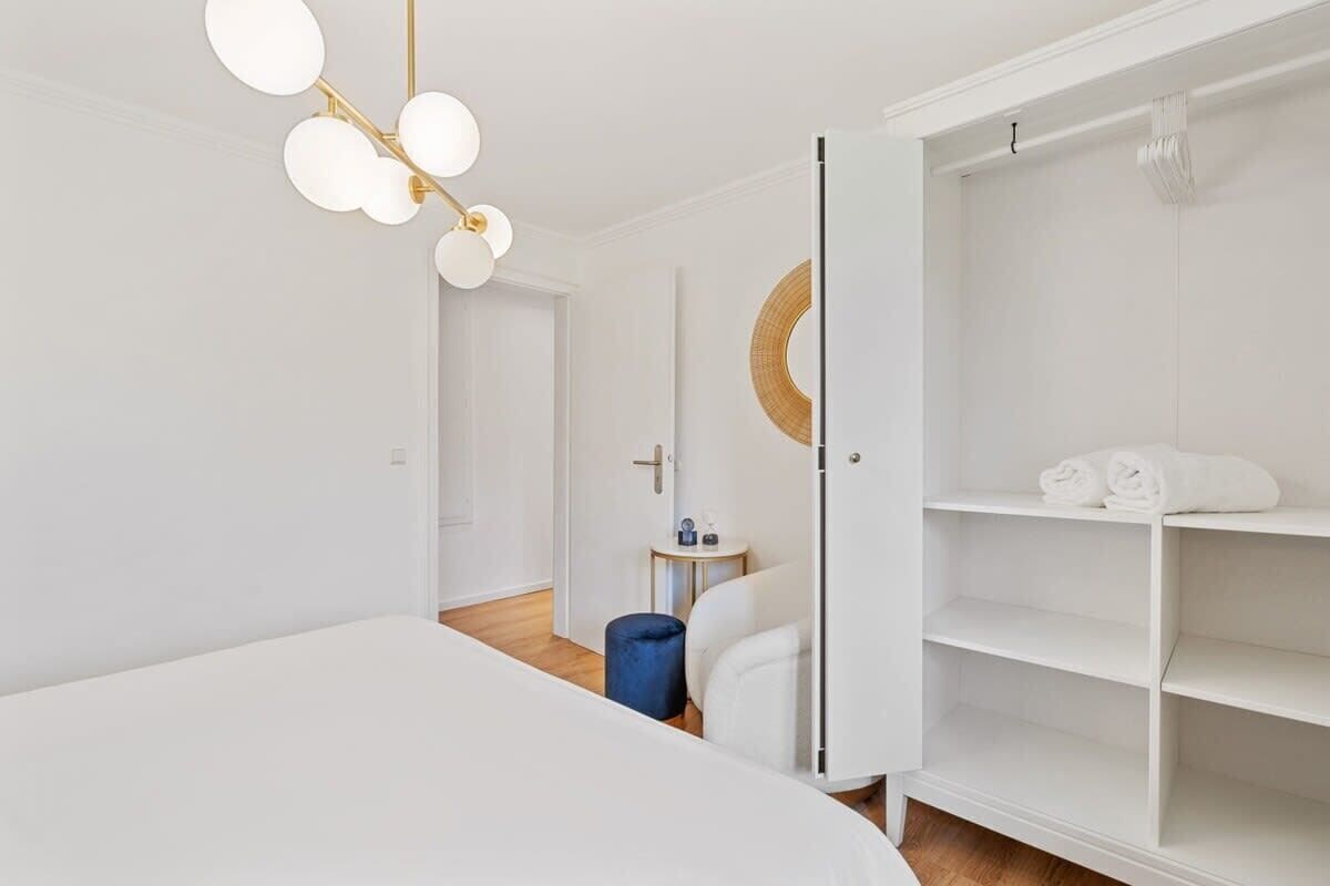 A modern hotel room with a large bed, a wardrobe, a small side table, and a unique circular mirror.
