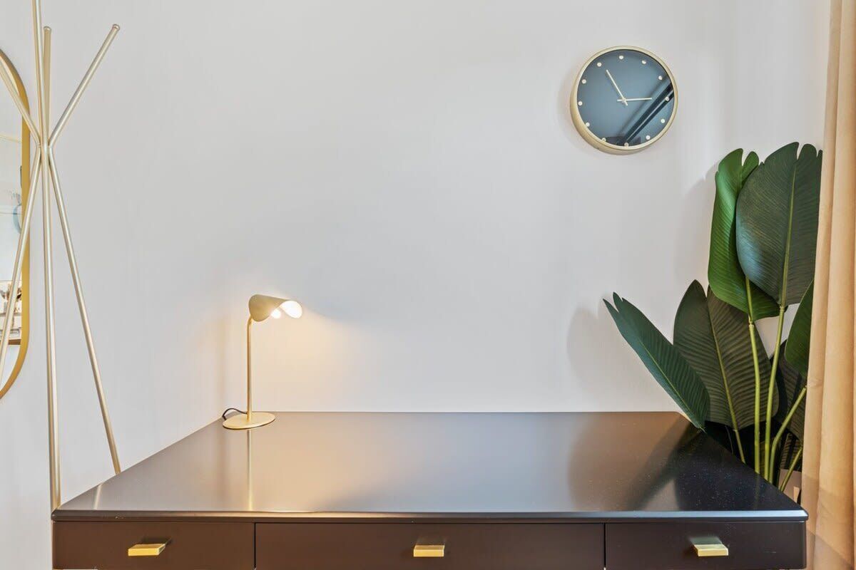 A modern desk with a lamp, a clock, and a plant.