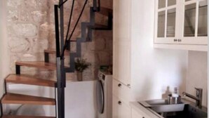 Una cocina con armarios blancos, un lavamanos de acero inoxidable y una escalera de madera.