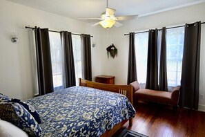 A bedroom with a bed, a chair, a ceiling fan, and a window with curtains.