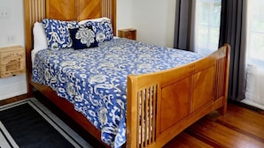 Un dormitorio con cama de madera, ventilador de techo, ventana con cortinas y una mesita de noche pequeña.