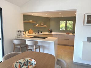 A modern kitchen with a central island, bar stools, and a dining table with a patterned cushion. - Villa MEERBLICK and Porto-Vecchio's Old Town, 4 bedrooms, infinity pool (Porto-Vecchio)