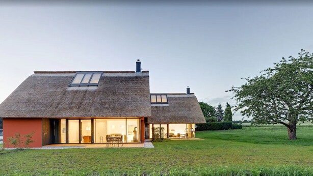 A modern house with a thatched roof, large glass windows, and a well-maintained lawn. - Thatched roof meets modernity; lake view, sauna, garden and much more... (Putbus)