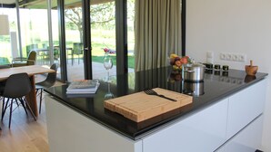 A modern kitchen with a large island, a dining area with a table and chairs, and a view of the outdoors. - Thatched roof meets modernity; lake view, sauna, garden and much more... (Putbus)