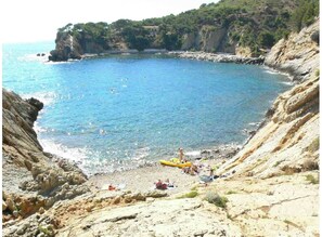 A coastal beach with rocky terrain and a clear blue sea.