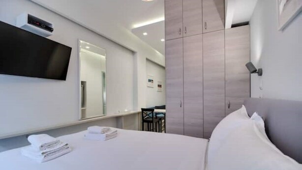 Een moderne hotelkamer met een groot bed, een flatscreen televisie aan de wand, een houten garderobe en een bureau met stoel.