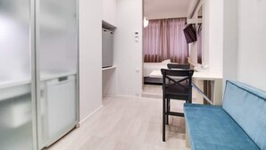 Een moderne hotelkamer met een schuifdeur, een kleine kitchenette, een bank en een raam met gordijnen.