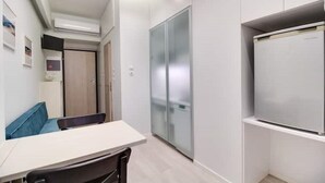 Een compacte keuken met een wit aanrecht, een inbouwkoelkast en een kast met een schuifdeur van glas.