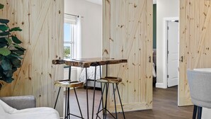 Una habitació amb una porta corredissa de fusta, un llit, una taula amb tamborets i una planta.