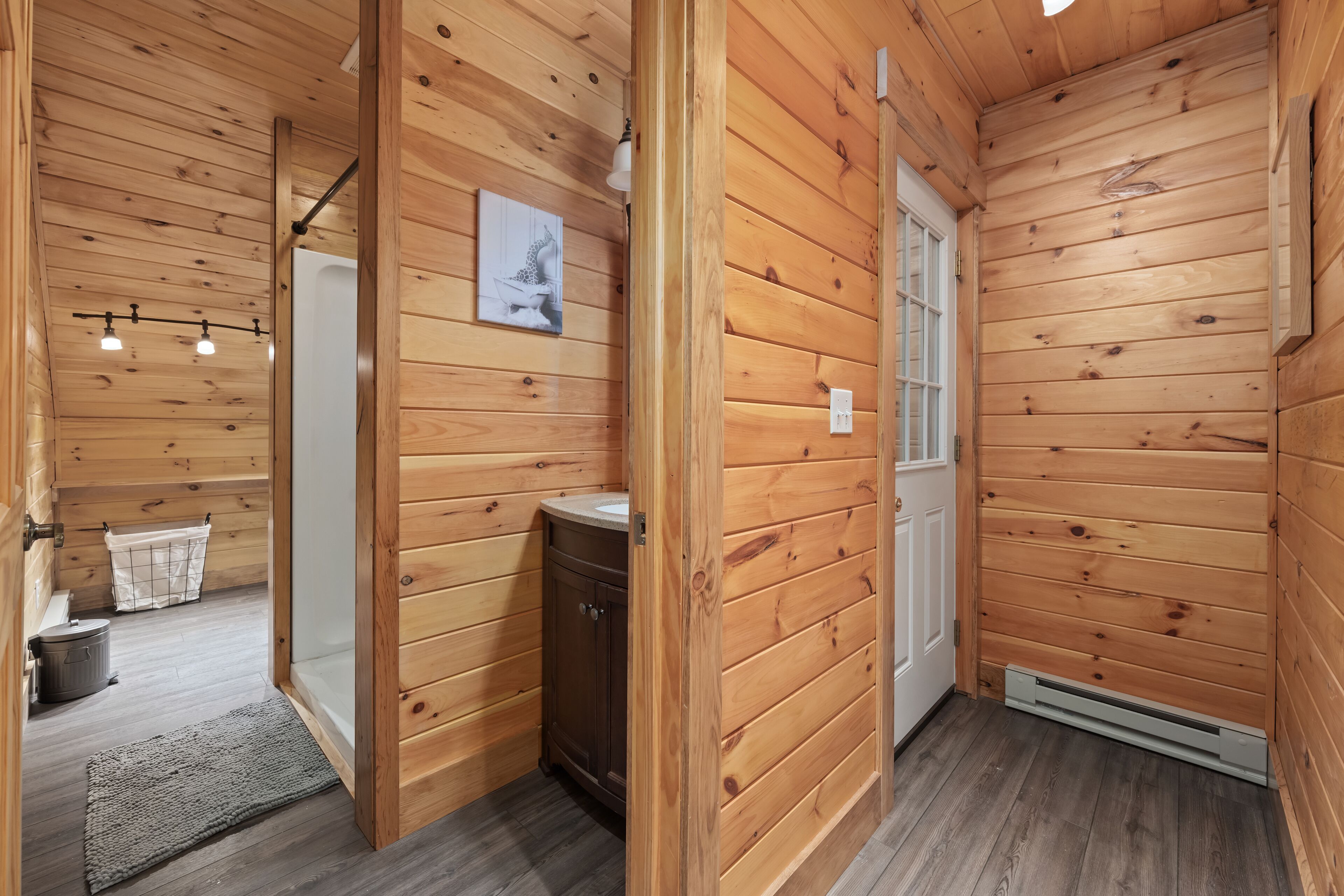 L’intérieur d’une cabane en bois, avec une porte en bois, un petit meuble, un porte-serviettes et un tableau accroché au mur.