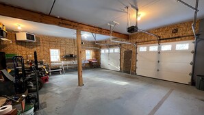 A garage with a concrete floor, wooden walls, and a white garage door. - Loft In the Pines, On Snowmobile Trail (Boonville)