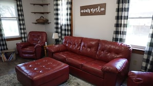 A living room with a red leather sofa, matching ottoman, a red leather armchair, and a wall-mounted sign that reads "our nest". - Cozy Farm house 1950's Era but with modern updates (New Enterprise)
