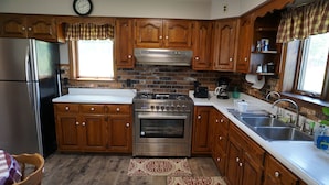 A kitchen with wooden cabinets, a stainless steel refrigerator, a gas stove, and a sink. - Cozy Farm house 1950's Era but with modern updates (New Enterprise)