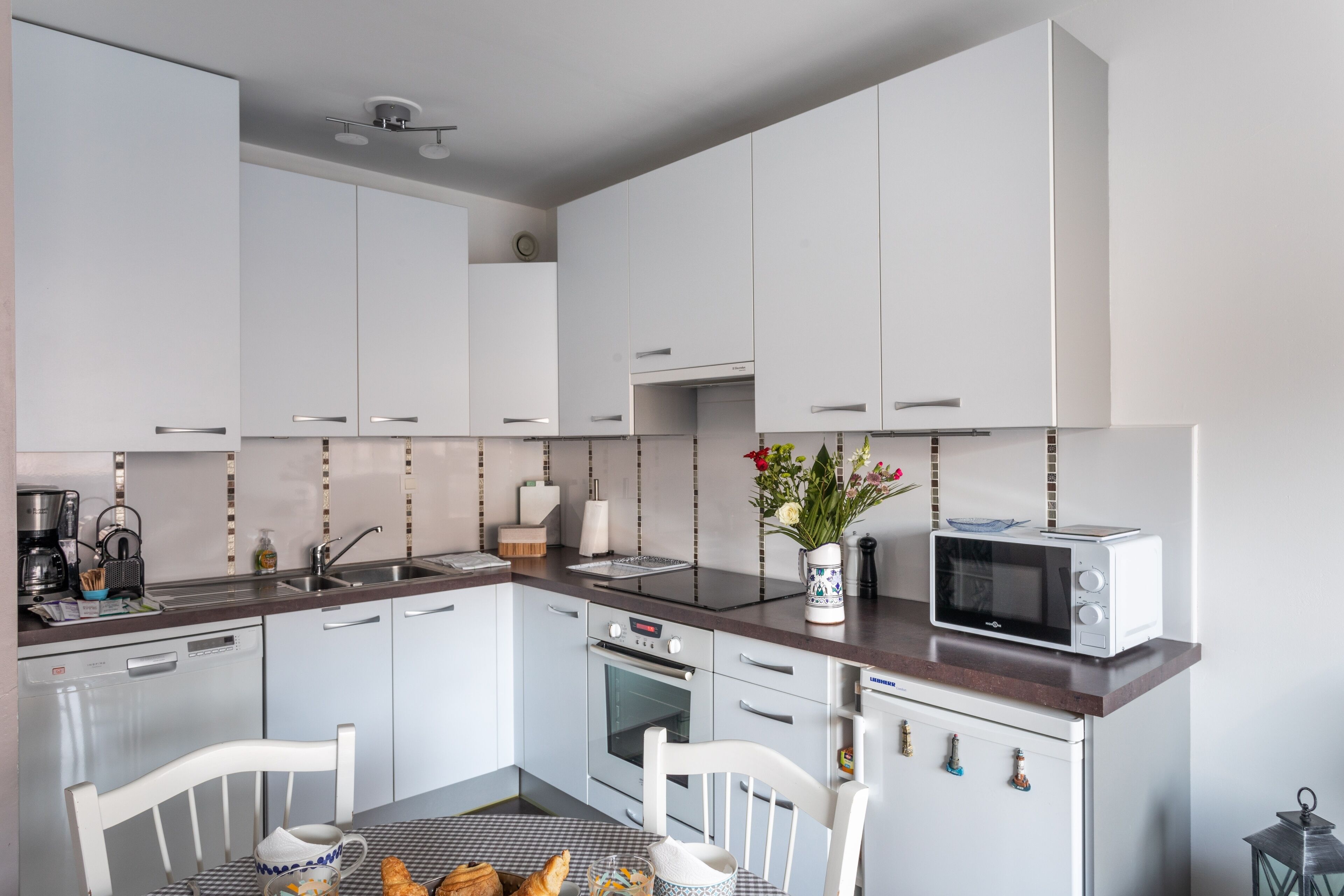 A modern kitchen with white cabinets, a microwave, and a dining table with chairs.