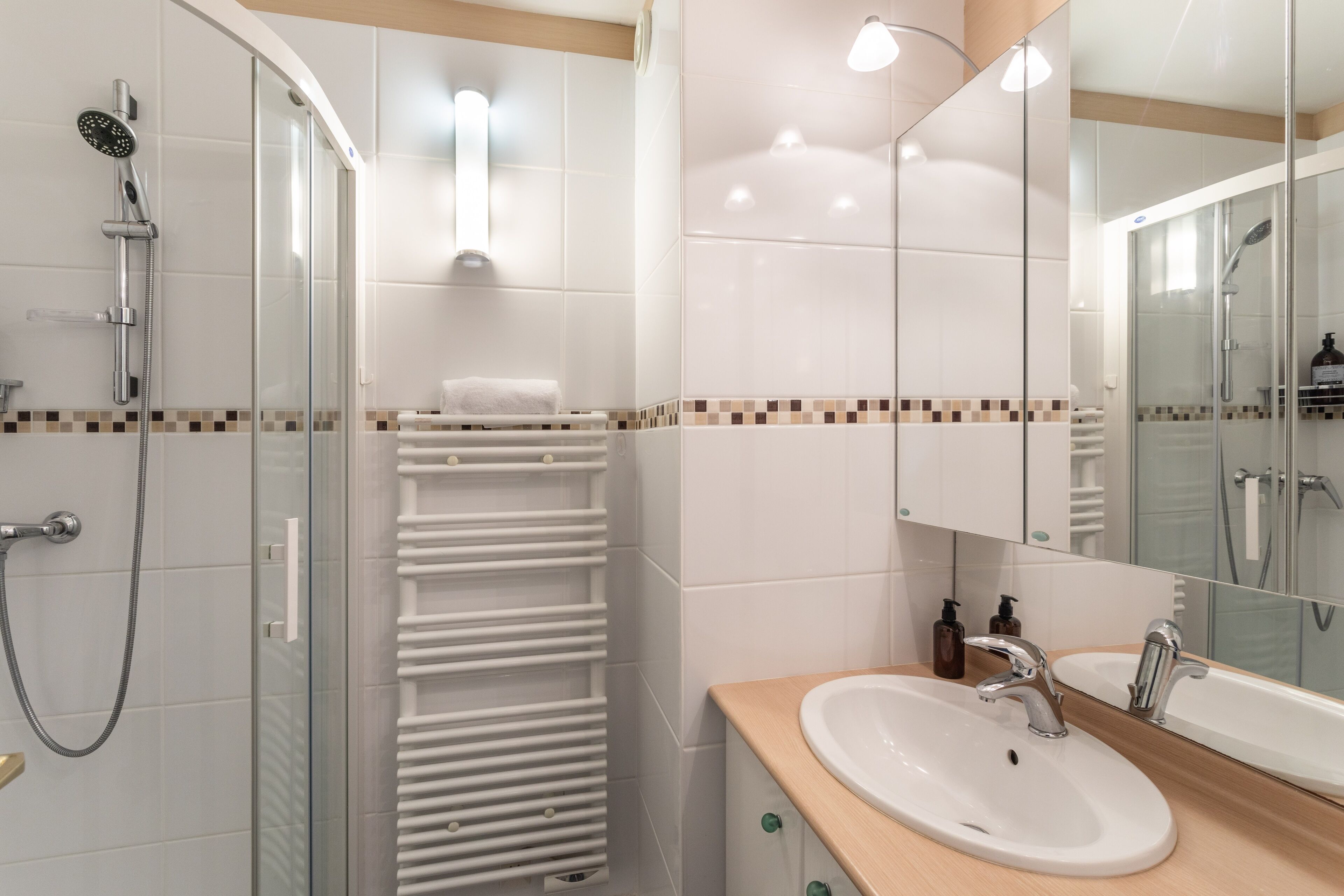 A modern bathroom with a glass-enclosed shower, a white sink with a wooden countertop, and a large mirror.