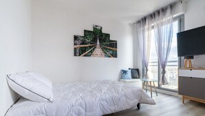 A bedroom with a bed, a TV, a painting, and a window with curtains. - Marée Tropicale - vue mer (Saint-Cast-le-Guildo)