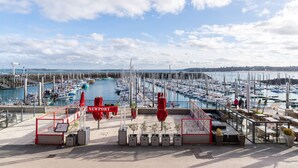 A marina with boats, a café area with outdoor seating, and a clear sky. - Marée Tropicale - vue mer (Saint-Cast-le-Guildo)