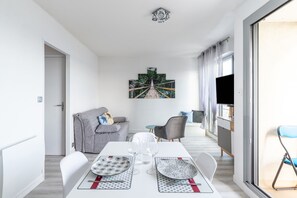 Ett modernt matområde med ett bord dukat för två personer, en grå soffa, en tv och en tavla som föreställer en bro.