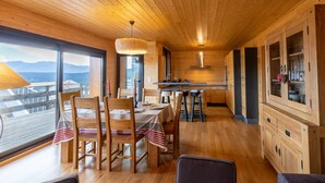 A wooden interior with a dining area, kitchen, and large windows offering a mountain view. - Adret - Two Bedroom Apartment, Sleeps 4 (Les Angles)