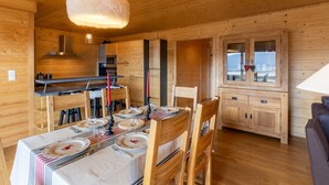 A wooden cabin interior with a dining area set for four, featuring a table with a striped tablecloth, wooden chairs, and a chandelier. - Adret - Two Bedroom Apartment, Sleeps 4 (Les Angles)