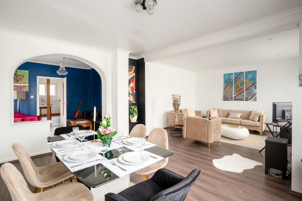 Un salon moderne avec un coin repas, comprenant une grande table dressée pour quatre personnes, un canapé beige et un téléviseur.